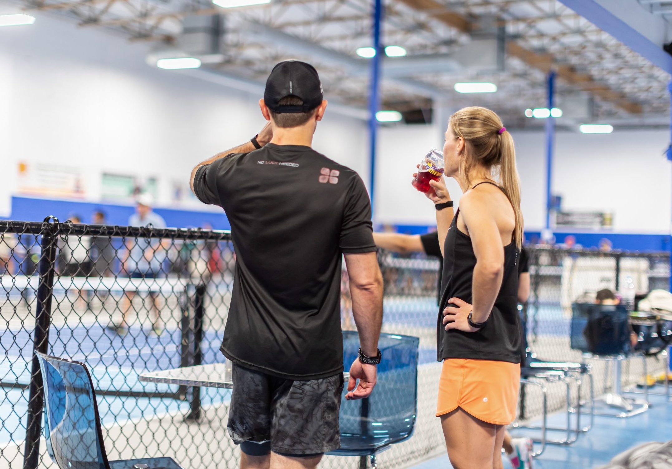 Players taking a break courtside with drinks at an indoor pickleball facility.
