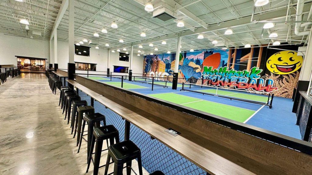 Indoor pickleball courts, courtside drink rail and OKC skyline mural at Northpark Pickleball in Oklahoma City